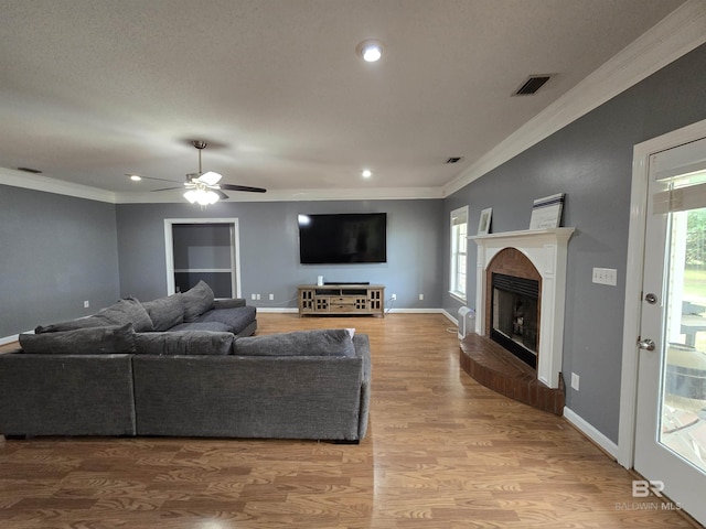 living room featuring crown molding, a brick fireplace, ceiling fan, and plenty of natural light