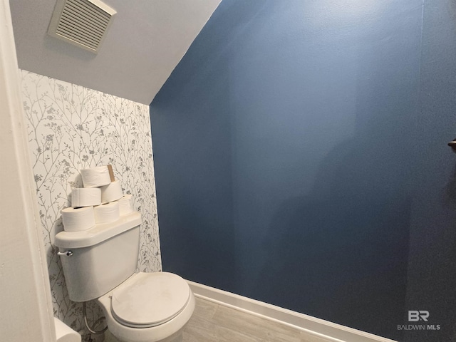bathroom featuring visible vents, wallpapered walls, toilet, vaulted ceiling, and wood finished floors