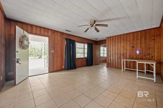 empty room featuring ceiling fan, wood walls, and light tile patterned floors