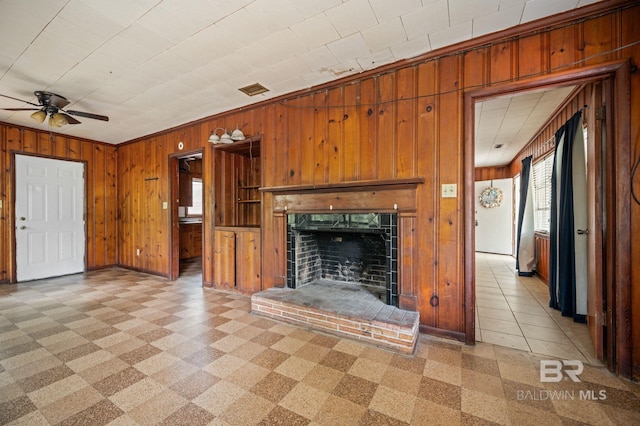 unfurnished living room featuring crown molding, ceiling fan, wooden walls, and a brick fireplace