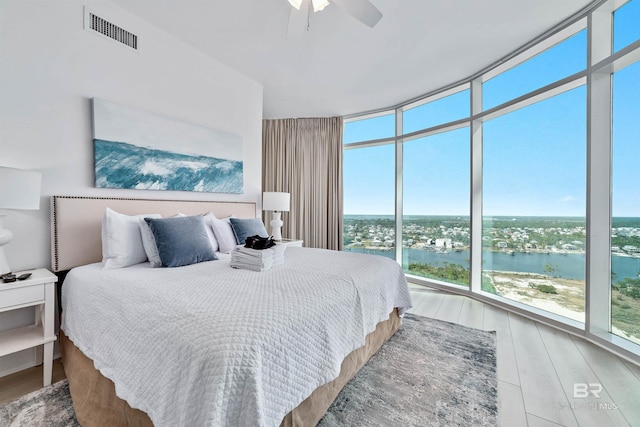 bedroom featuring visible vents, a water view, wood finished floors, floor to ceiling windows, and ceiling fan