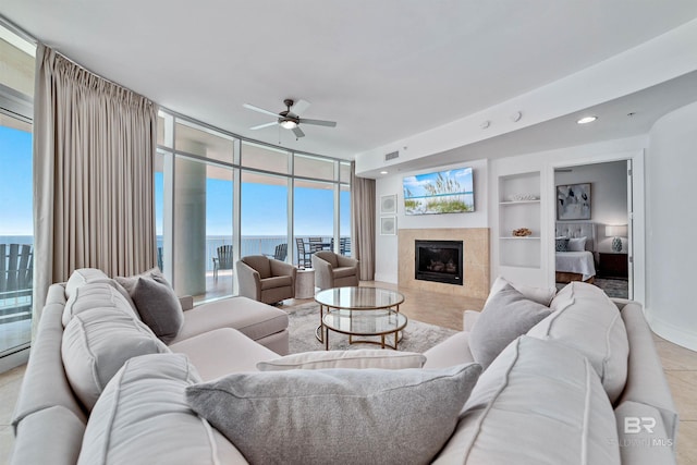 living room featuring a wall of windows, built in features, visible vents, a fireplace, and ceiling fan