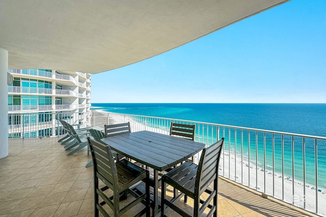 balcony featuring a beach view, outdoor dining area, and a water view