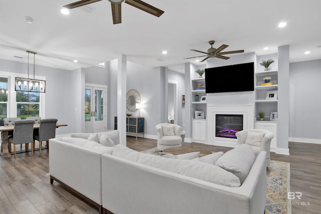 living room with built in shelves, french doors, ceiling fan with notable chandelier, and light wood-type flooring