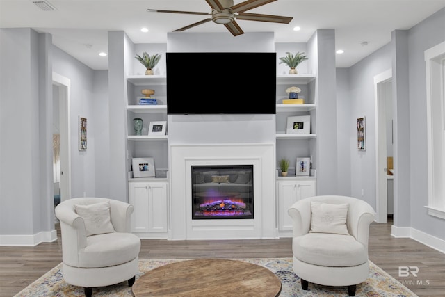 living room with built in shelves, ceiling fan, and wood-type flooring