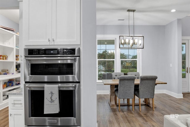 kitchen with a chandelier, white cabinetry, stainless steel double oven, and decorative light fixtures