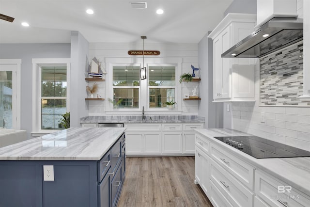 kitchen with black electric stovetop, wall chimney exhaust hood, sink, white cabinets, and a kitchen island