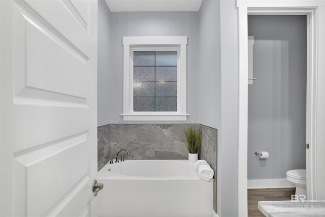 bathroom with hardwood / wood-style floors, a bath, and toilet