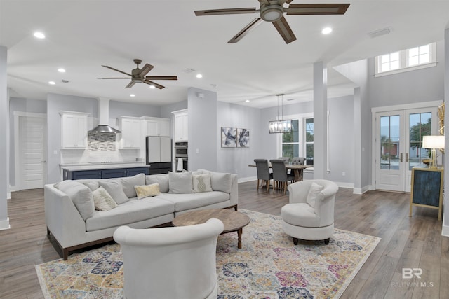 living room featuring ceiling fan with notable chandelier, french doors, and light hardwood / wood-style flooring