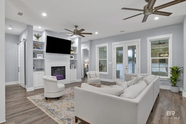 living room featuring french doors, ceiling fan, wood-type flooring, a barn door, and built in features