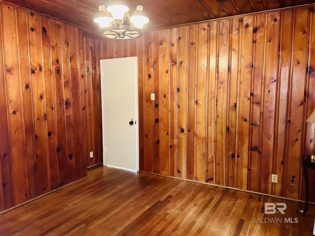 unfurnished room with wood-type flooring, a chandelier, and wood walls