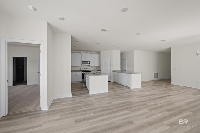 kitchen with a center island with sink, visible vents, open floor plan, stainless steel appliances, and light wood-style floors