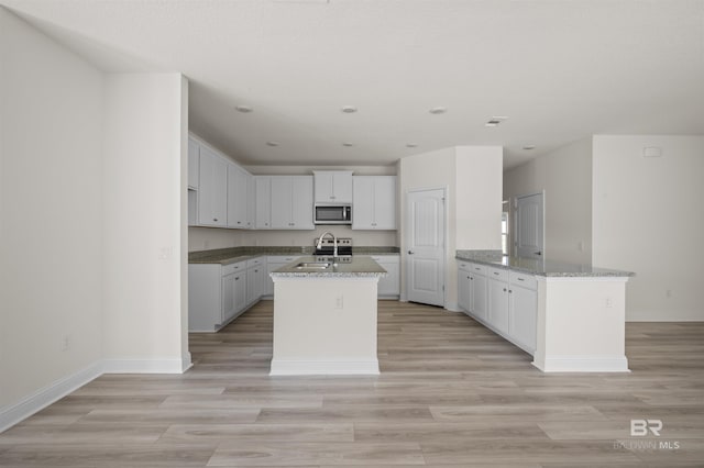 kitchen with light wood-style flooring, stainless steel microwave, light stone counters, a peninsula, and a sink