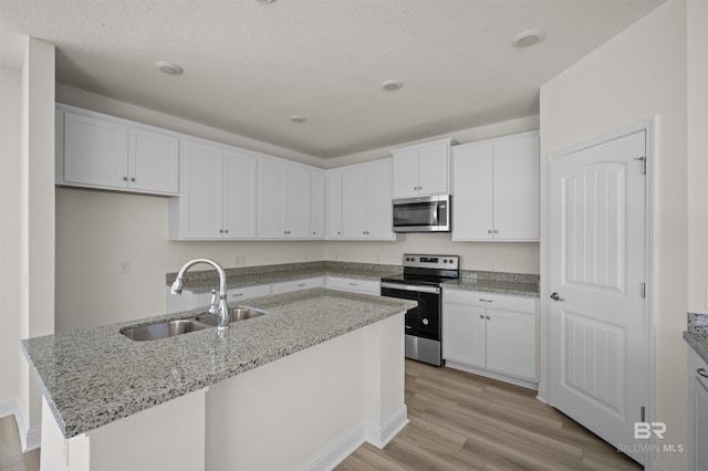 kitchen with white cabinets, light stone counters, stainless steel appliances, and a sink