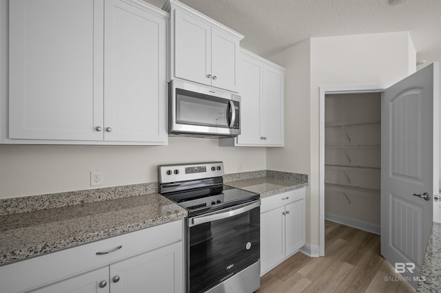 kitchen with a textured ceiling, light stone counters, white cabinetry, appliances with stainless steel finishes, and light wood finished floors