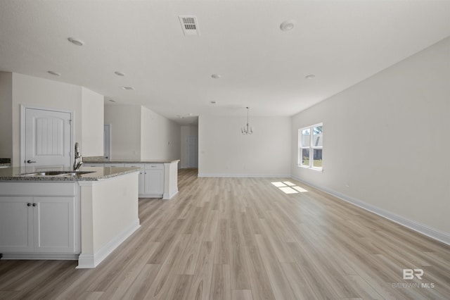 kitchen featuring stone counters, a center island with sink, open floor plan, white cabinets, and a sink