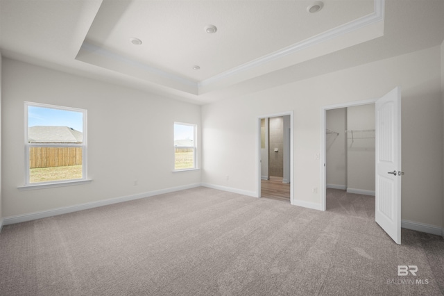 unfurnished bedroom featuring light carpet, baseboards, a tray ceiling, a walk in closet, and a closet
