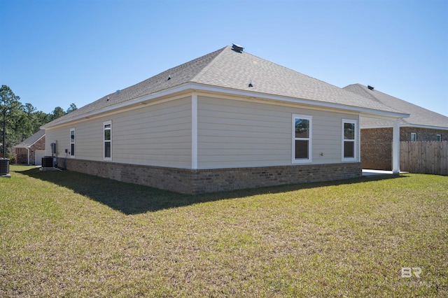 back of house with central AC, brick siding, a shingled roof, fence, and a lawn