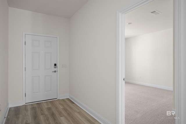 hall with visible vents, baseboards, and wood finished floors