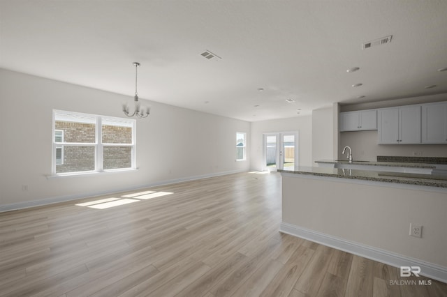 kitchen with a sink, stone counters, visible vents, and light wood-style floors