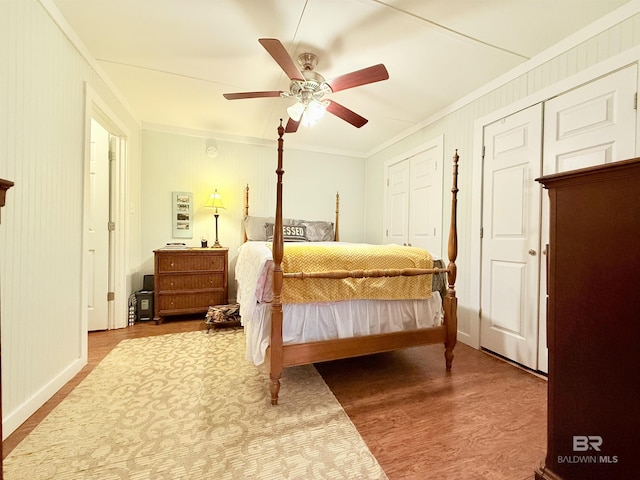 bedroom with ceiling fan, wood finished floors, ornamental molding, and multiple closets