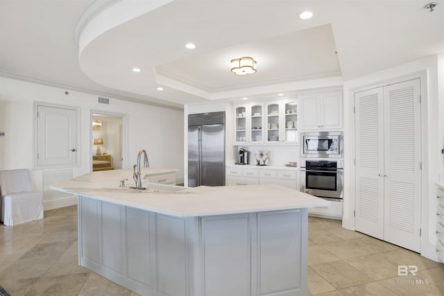 kitchen with a sink, glass insert cabinets, built in appliances, white cabinetry, and a raised ceiling