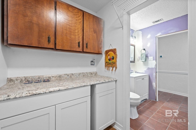 bathroom featuring tile patterned flooring, vanity, toilet, and a textured ceiling