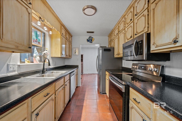 kitchen featuring appliances with stainless steel finishes, light brown cabinetry, a textured ceiling, dark tile patterned floors, and sink