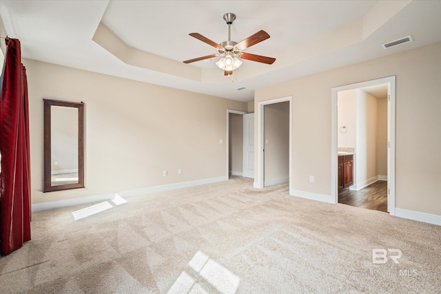 unfurnished bedroom with carpet, ensuite bath, a raised ceiling, and ceiling fan