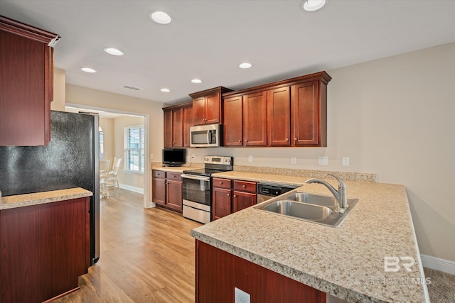 kitchen with kitchen peninsula, appliances with stainless steel finishes, light wood-type flooring, and sink