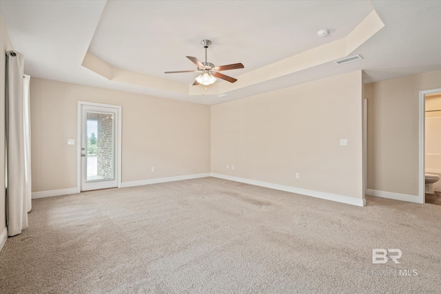 empty room with ceiling fan, light carpet, and a tray ceiling