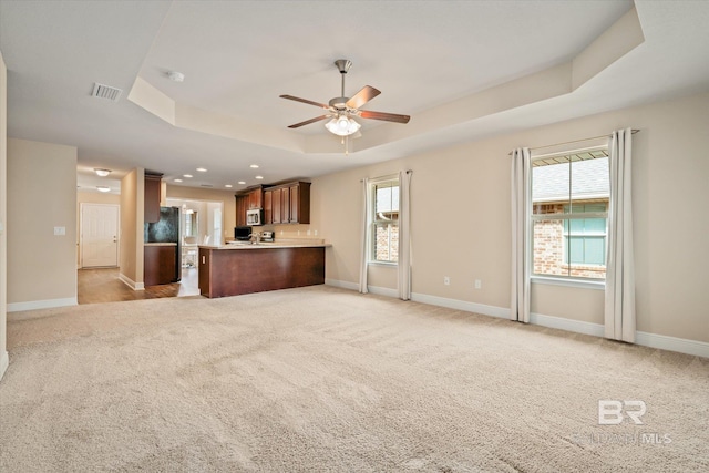 unfurnished living room with a raised ceiling, ceiling fan, and light colored carpet