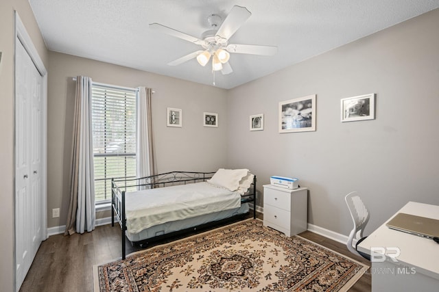 bedroom featuring dark wood-style flooring, a closet, a ceiling fan, a textured ceiling, and baseboards