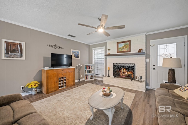 living area featuring visible vents, wood finished floors, crown molding, a textured ceiling, and a fireplace