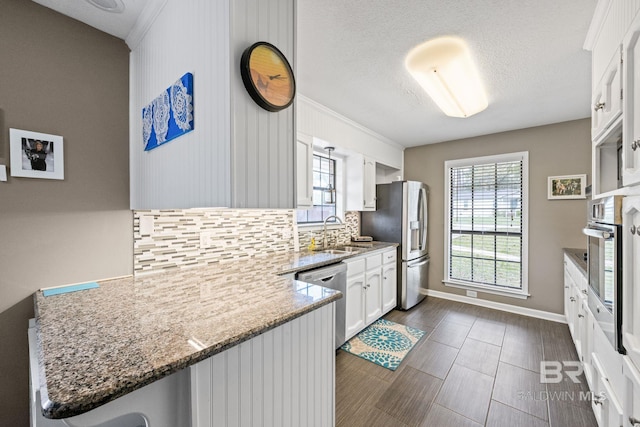 kitchen featuring white cabinets, appliances with stainless steel finishes, a peninsula, a sink, and backsplash