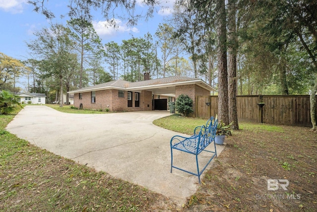 rear view of property with brick siding, a chimney, fence, a carport, and driveway