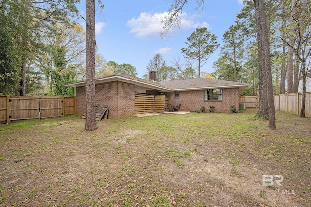 back of property featuring brick siding, a lawn, a chimney, and a fenced backyard