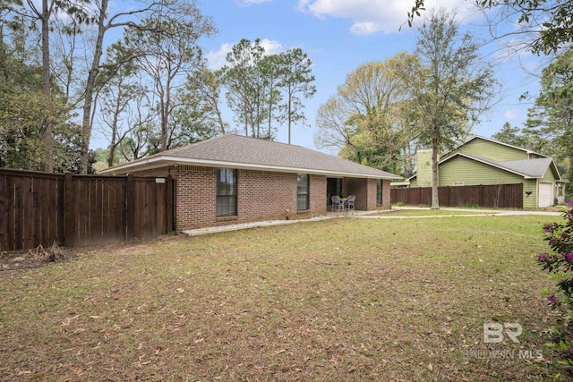 exterior space featuring a shingled roof, brick siding, a lawn, and a fenced backyard