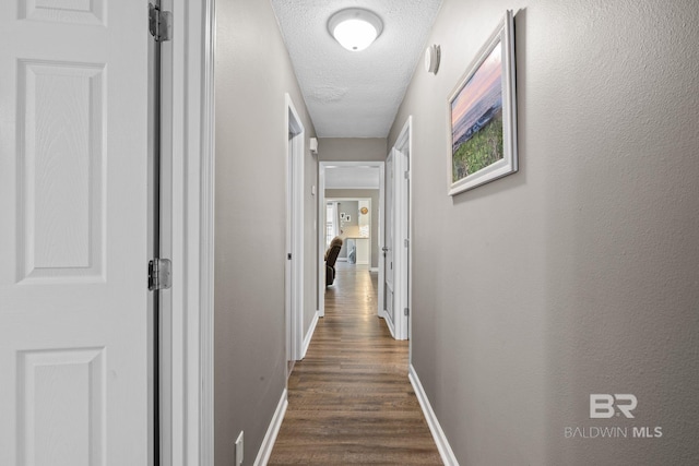 hallway featuring a textured ceiling, dark wood-style flooring, and baseboards