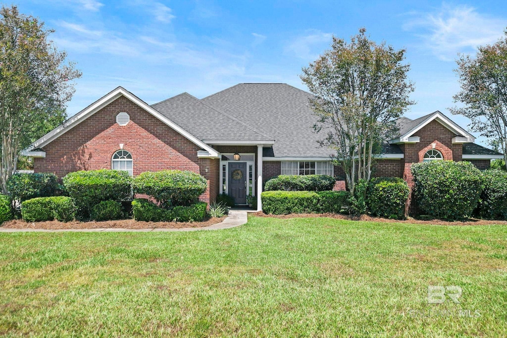 view of front facade with brick siding, roof with shingles, and a front lawn