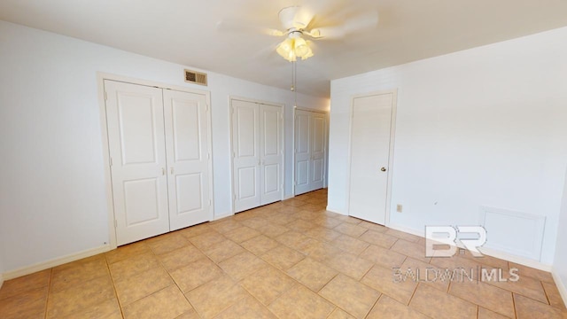 unfurnished bedroom featuring two closets, ceiling fan, and light tile patterned floors