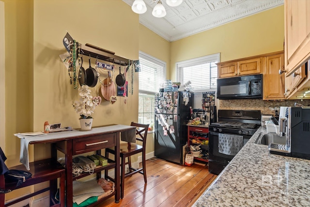 kitchen with light stone counters, ornamental molding, black appliances, light hardwood / wood-style floors, and decorative backsplash