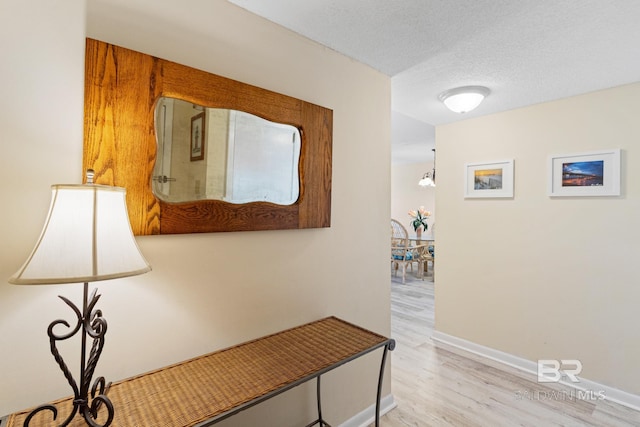 hall featuring a textured ceiling, baseboards, and wood finished floors