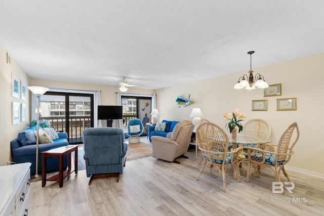 living area featuring baseboards, light wood-style floors, ceiling fan with notable chandelier, and a textured ceiling