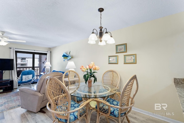 dining space featuring baseboards, a textured ceiling, an inviting chandelier, and light wood finished floors