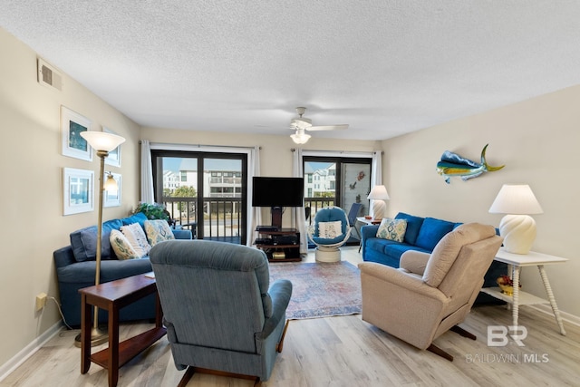 living area featuring baseboards, light wood-style floors, visible vents, and a textured ceiling