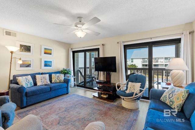 living room featuring visible vents, a textured ceiling, wood finished floors, and a ceiling fan