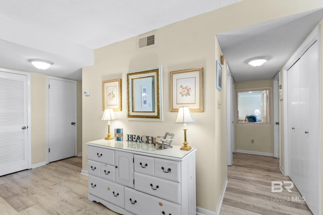 hall with light wood finished floors, visible vents, a textured ceiling, and baseboards