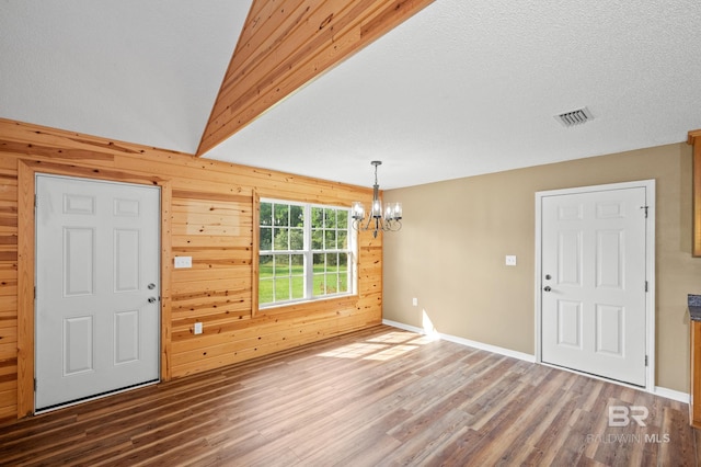 entrance foyer featuring vaulted ceiling, wood walls, a textured ceiling, hardwood / wood-style flooring, and a notable chandelier