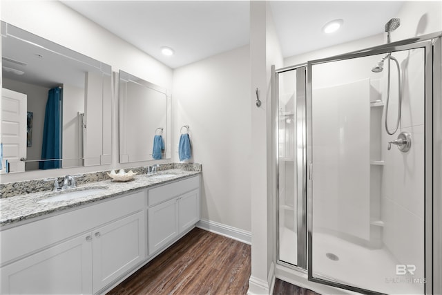bathroom featuring wood finished floors, a sink, a stall shower, double vanity, and baseboards